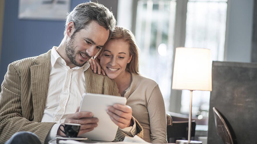 Smiling couple sitting close together looking at a tablet in a cozy setting