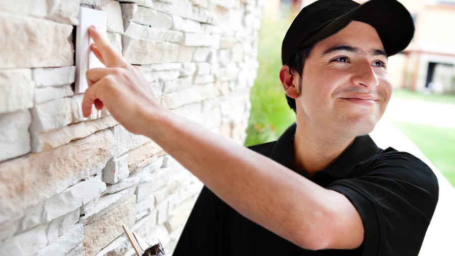 Delivery person in a black cap pressing a doorbell on a stone wall