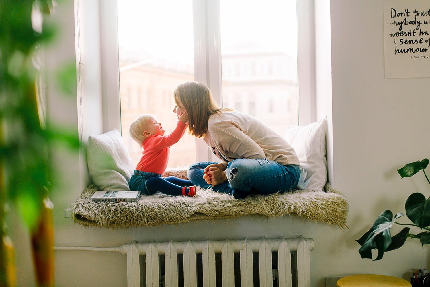Mother and baby sitting on a windowsill, the baby touching her face playfully