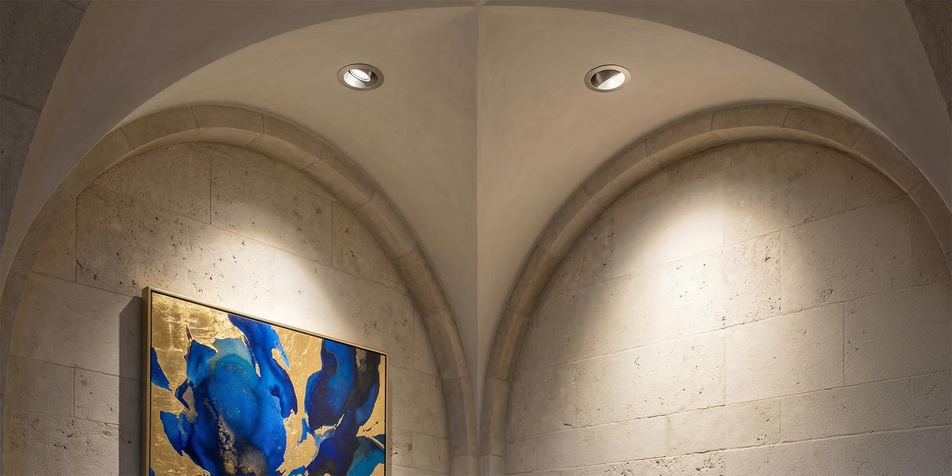 Recessed ceiling downlights illuminating an arched stone wall with abstract art