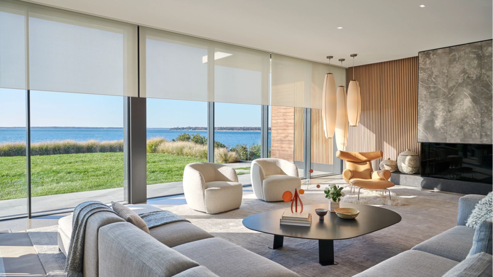 A modern, sunlit living room featuring floor-to-ceiling windows with a lake view and automated roller shades.